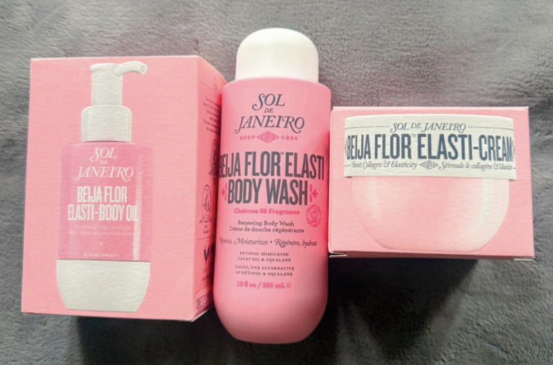 A free-sample haul of Sol de Janeiro Beija Flor products — body oil, body wash and Elasti-Cream — laid out on a grey blanket